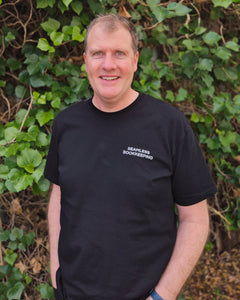Glen - Bookkeeper at Seamless Bookkeeping (a bookkeeping firm based in Geelong Victoria servicing clients Australia wide) wearing a black t-shirt with 'Seamless Bookkeeping' text against a green leafy background