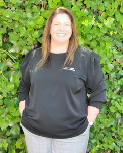 Lara - Senior Bookkeeper at Seamless Bookkeeping (a bookkeeping firm based in Geelong Victoria servicing clients Australia wide) wearing a black t-shirt with 'Seamless Bookkeeping' text against a green leafy background